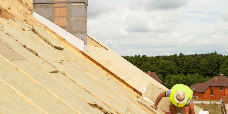 Roofer builder worker installing roof insulation material on new house
