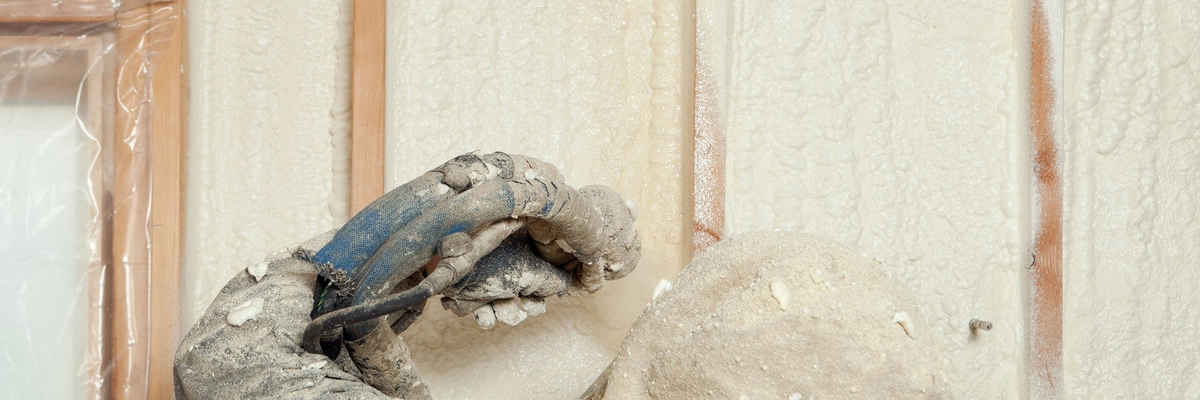 Worker spraying expandable foam insulation between wall studs